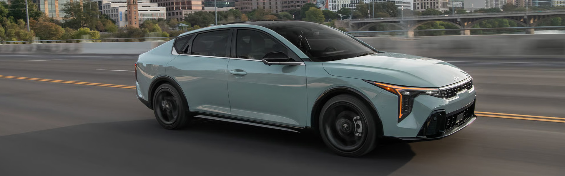 Light green Kia K4 sedan driving on a city road.