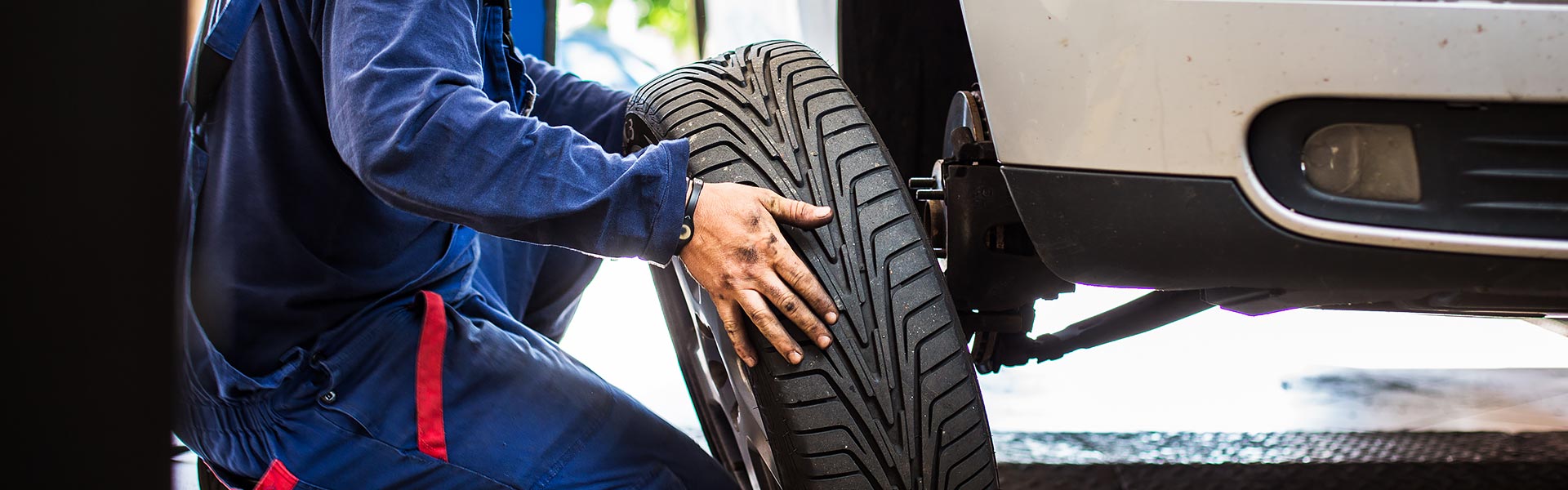 Mechanic mounting a tire onto a white vehicle.