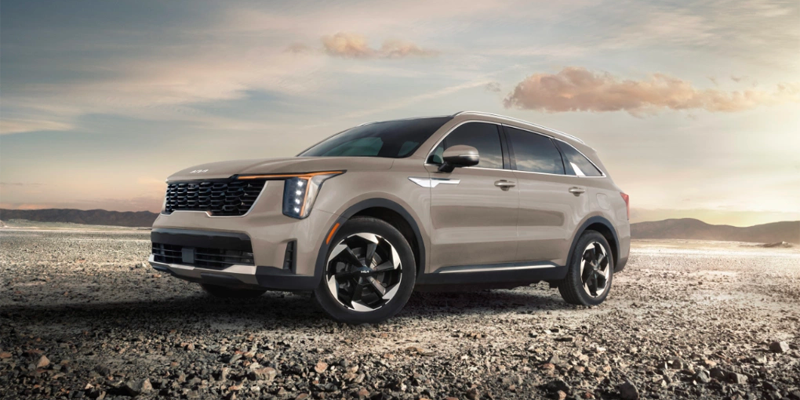 A beige Kia is parked on a rocky desert landscape under a warm