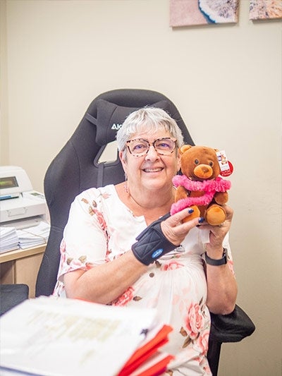 person sitting at a desk holds up a brown teddy bear