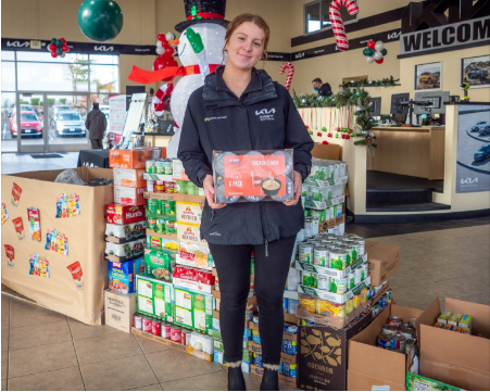 Kia employee holding a donation pack next to a large food collection.