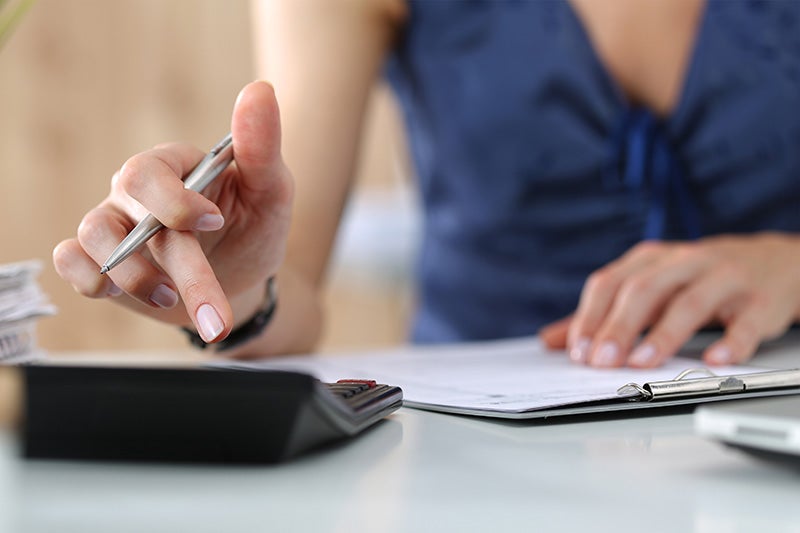 Close-up of hands using a calculator and pen over paperwork.
