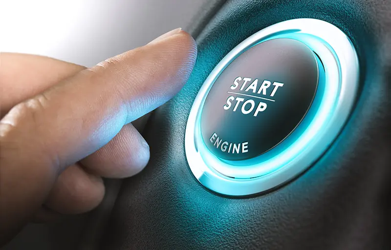 A finger reaching to press a glowing blue Start Stop Engine button.