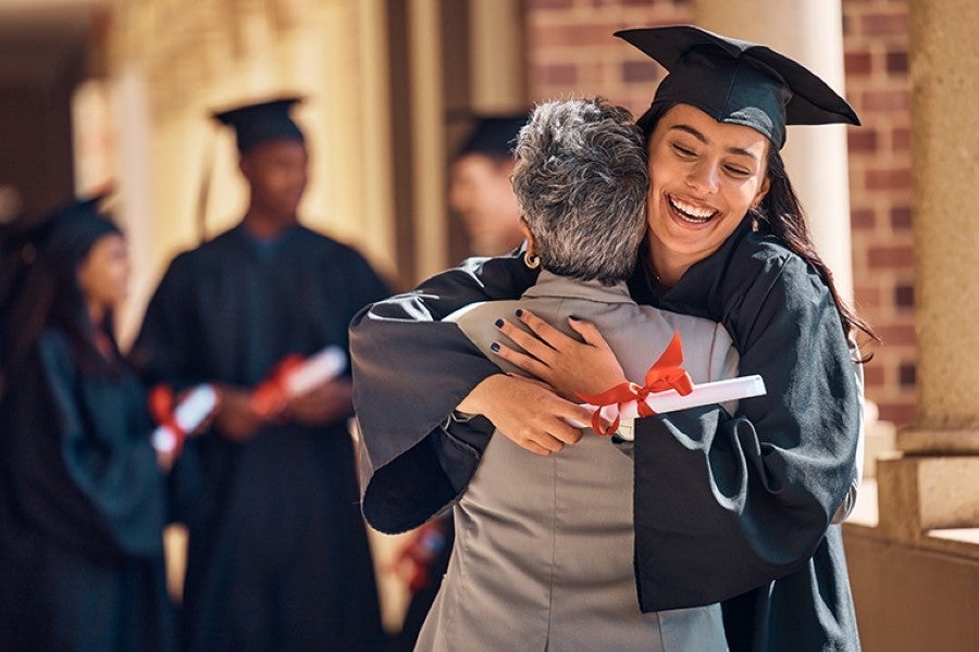 A joyful graduate in a cap and gown hugging a proud family member