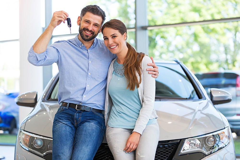 A happy couple posing with new car keys in a bright dealership.