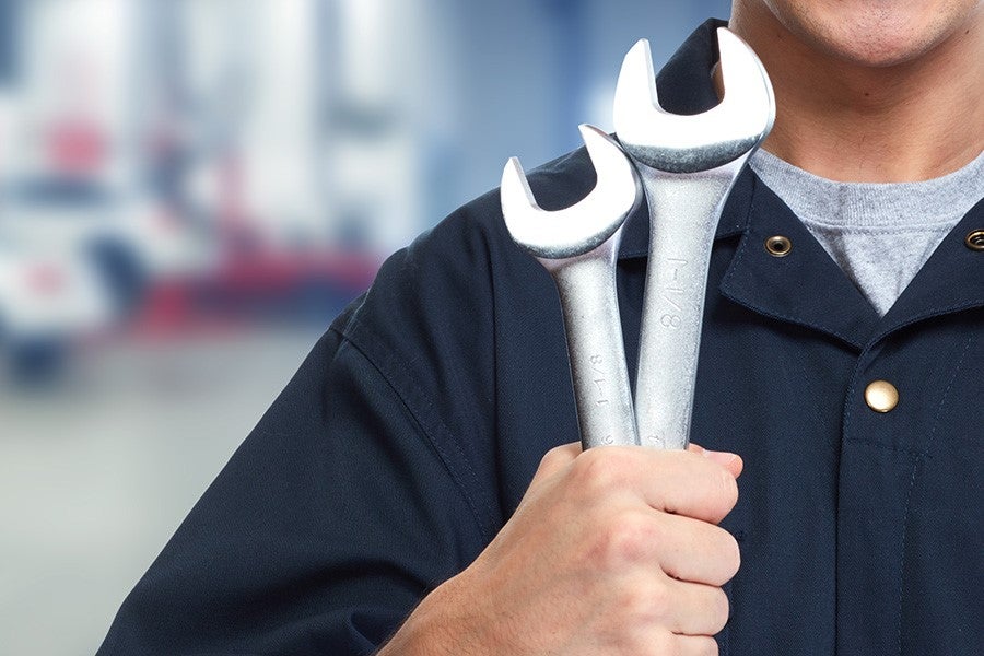 A service technician holding two large metal wrenches in a workshop environment