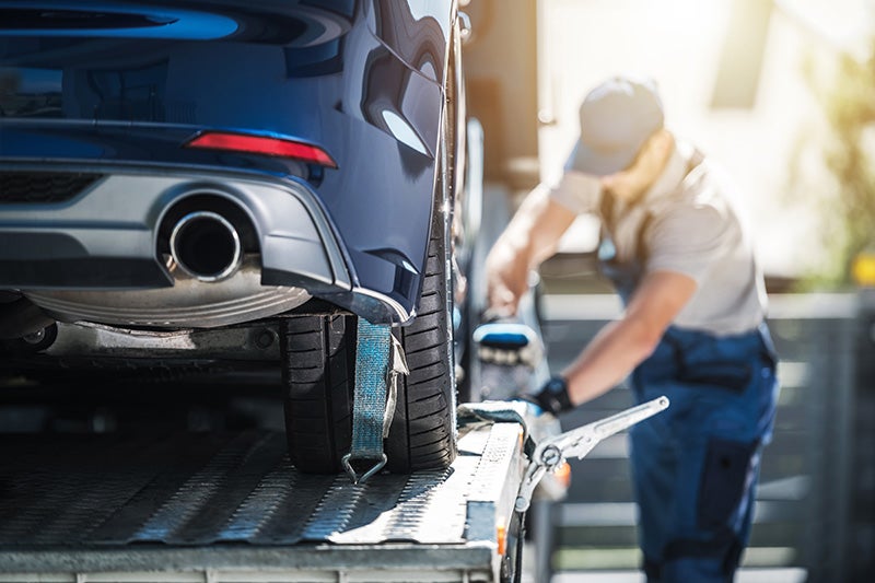 A worker securing a car onto a flatbed tow truck with straps